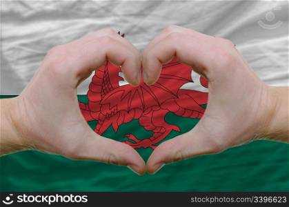 Gesture made by hands showing symbol of heart and love over wales flag