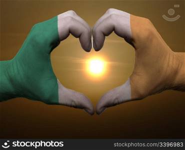 Gesture made by ireland flag colored hands showing symbol of heart and love during sunrise