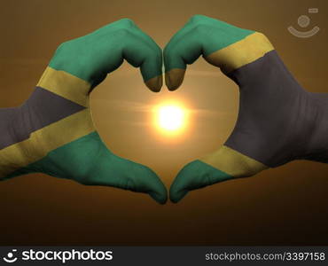 Gesture made by jamaica flag colored hands showing symbol of heart and love during sunrise