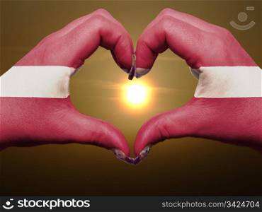 Gesture made by latvia flag colored hands showing symbol of heart and love during sunrise