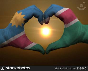 Gesture made by namibia flag colored hands showing symbol of heart and love during sunrise