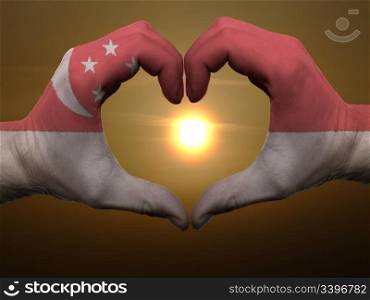 Gesture made by singapore flag colored hands showing symbol of heart and love during sunrise