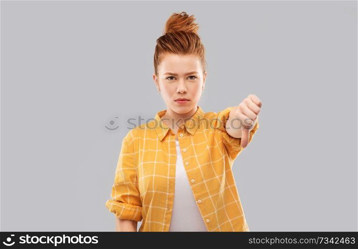 gesture, negative emotions and people concept - angry red haired teenage girl showing thumbs down over grey background. angry red haired teenage girl showing thumbs down