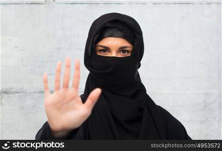 gesture, religious prohibition and people concept - muslim woman in hijab showing stop sign over gray concrete wall background. muslim woman in hijab showing stop sign