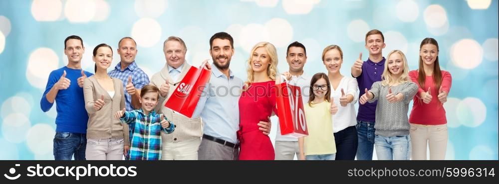 gesture, sale, shopping and people concept - group of smiling men, women and boy showing thumbs up over blue holidays lights background