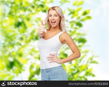gesture, summer and people concept - happy smiling young woman in white top and jeans showing thumbs up over green natural background. happy young woman showing thumbs up