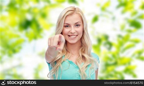 gesture, summer and people concept - happy smiling young woman or teenage girl pointing finger to you over green natural background
