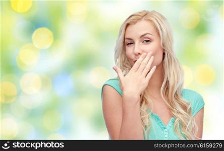 gesture, summer and people concept - smiling young woman or teenage girl covering her mouth with hands over green lights background