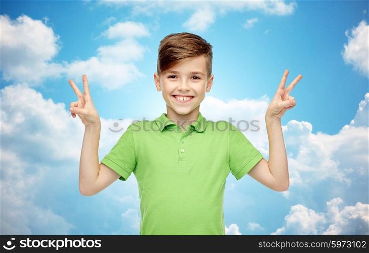 gesture, triumph, childhood, fashion and people concept - happy smiling boy in green polo t-shirt showing peace or victory hand sign over blue sky and clouds background