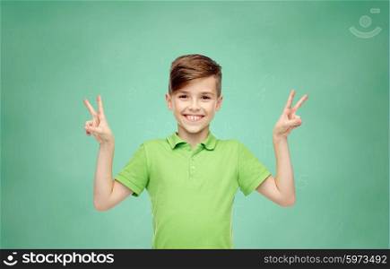 gesture, triumph, childhood, fashion and people concept - happy smiling boy in green polo t-shirt showing peace or victory hand sign over green school chalk board background