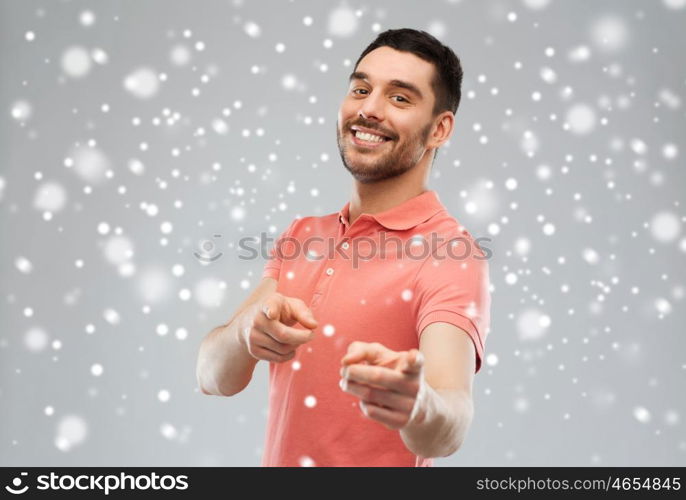 gesture, winter, christmas and people concept - happy smiling young man pointing finger to you over snow on gray background
