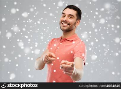 gesture, winter, christmas and people concept - happy smiling young man pointing finger to you over snow on gray background