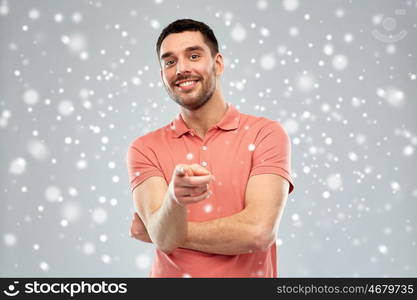 gesture, winter, christmas and people concept - happy smiling young man pointing finger to you over snow on gray background