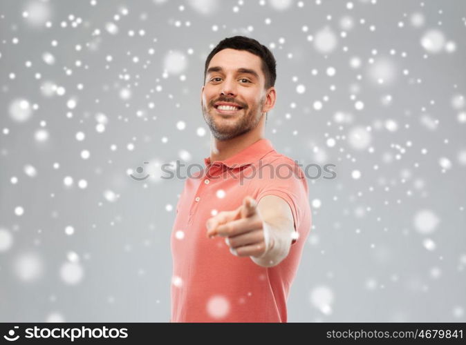 gesture, winter, christmas and people concept - happy smiling young man pointing finger to you over snow on gray background