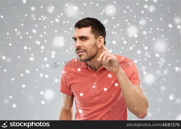 gesture, winter, christmas and people concept - latin man having hearing problem listening to something over snow on gray background