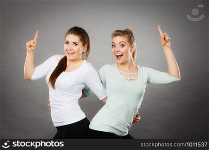 Gestures, having idea concept. Happy two women pointing up with finger. Studio shot on light dark background. Happy women pointing up with one finger.