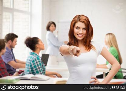 gestures, school and education concept - happy teenager at school in white t-shirt pointing at you
