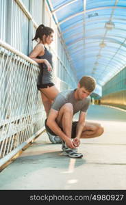 Getting ready for jogging. Front view of young man and woman tying shoelaces and relaxing while being outdoors