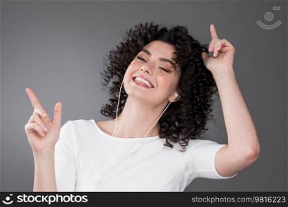 Getting rid of worried with good tunes in ears. Pleased attractive young woman listening music in earphones smiling dancing. Young woman listening music in earphones