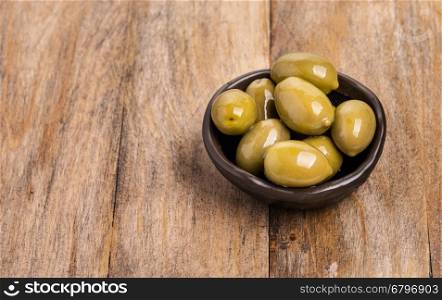 giant green olives in olive bowl on wood background, shallow focus