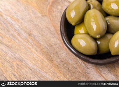 giant green olives in olive bowl on wood background, shallow focus