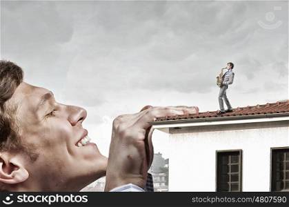 Giant man looking on saxophonist playing. Young man on building roof playing saxophone