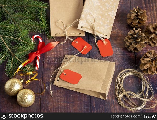 Gift bag made of handmade kraft paper on a wooden background in a Christmas style, decorated with Christmas tree balls, cones, a ball of rope, fir branches. Christmas, New Year, winter holiday. Kraft package, holiday concept, top view, flat lay.Mocap.. Gift bag made of handmade kraft paper on a wooden background in a Christmas style, decorated with Christmas tree balls, cones, a ball of rope, fir branches. Christmas, New Year, winter holiday.