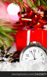 gift box and clock on snow with christmas tree branch on blurred background