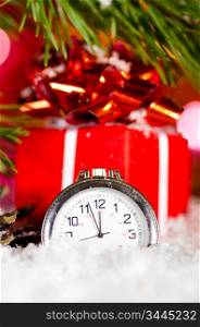 gift box and clock on snow with christmas tree branch on blurred background