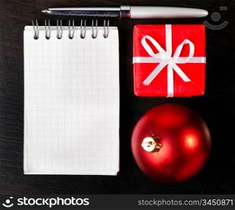 gift box and decorative christmas ball with notepad on dark table