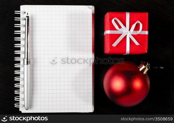 gift box and decorative christmas ball with notepad on dark table