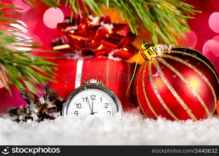 gift box, ball and clock on snow with christmas tree branch on blurred background