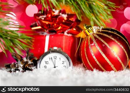 gift box, ball and clock on snow with christmas tree branch on blurred background