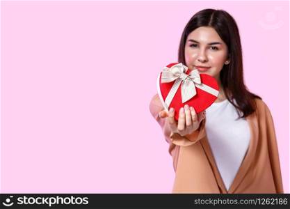 gift box in the shape of a heart in the hands of a young Asian girl. on a pink isolated background. focus on the box
