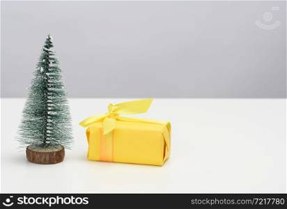 gift box is wrapped in yellow paper and a decorative Christmas tree on a white table. Festive background