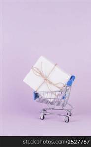 gift box tied with string shopping cart pink background