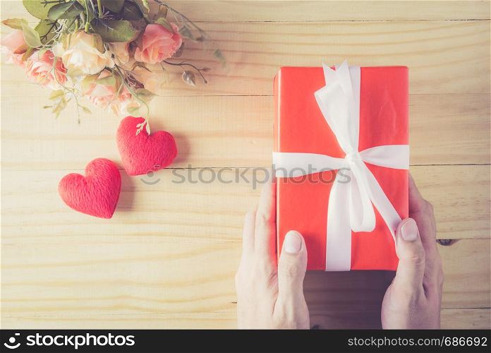 Gift box white bow ribbon on hand and heart with flower on wood table background top view, february of valentine's day in concept.