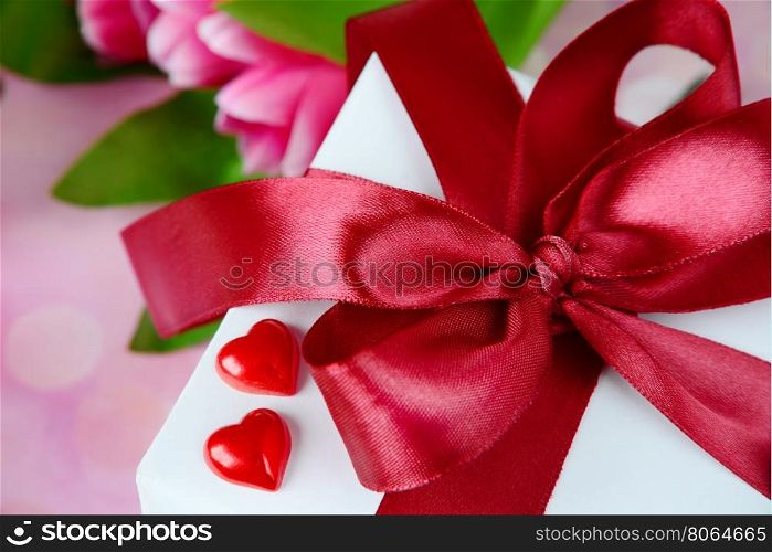 Gift box with a satin red bow and two scarlet hearts