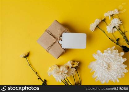 gift box with blank tag and flowers is placed on yellow background