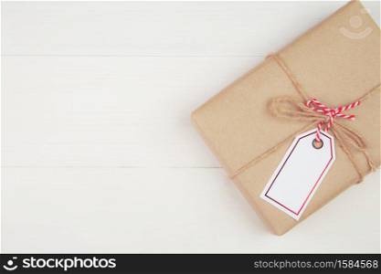 Gift box with kraft paper and tag or label on wooden table in Christmas day or holiday, present box for anniversary celebration with copy space, celebrate and festive, top view, flat lay.