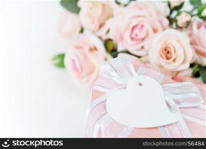 Gift box with label, ribbon and pink rose flowers on a light background