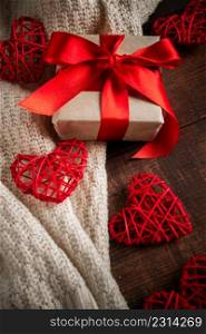 Gift box with red ribbon and hearts. Gift for Valentine&rsquo;s Day in a box with a red ribbon on the background of hearts and a cozy knitted pullover, vertical photo. Gift box with red ribbon and hearts.