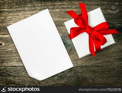 Gift box with red ribbon bow and paper sheet for Your text or design