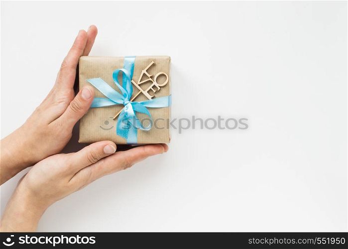 Gift box wrapped in brown paper with blue ribbon in womans hands on white background. Top view. Flat lay. Gift box wrapped in brown paper with blue ribbon in womans hands on white background. Top view. Copyspace