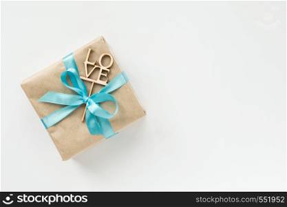 Gift box wrapped in brown paper with blue ribbon on white background. Top view. Flat lay. Gift box wrapped in brown paper with blue ribbon on white background. Top view. Copyspace