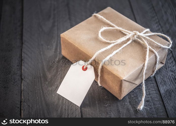 Gift box, wrapped in brown vintage paper and tied with white flax string, on an old black wooden table.