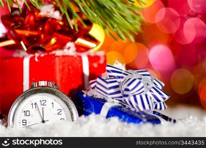 gift boxes and clock on snow with christmas tree branch on blurred background