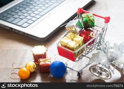 Gift boxes in shopping cart and Christmas decorations with laptop computer on wood table, Online shopping