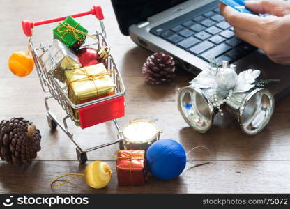 Gift boxes in shopping cart and Christmas decorations, Woman holding credit card on laptop computer for online shopping