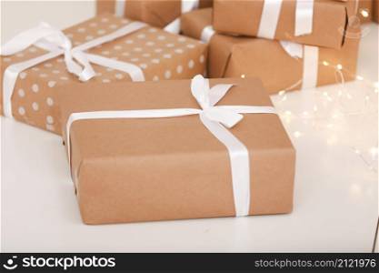 Gift boxes on white wood background. Presents in craft paper decorated with stylish elegant white satin ribbon bows. Christmas and any other holidays concept.. Gift boxes on white wood background. Presents in craft paper decorated with stylish elegant white satin ribbon bows. Christmas and any other holidays concept
